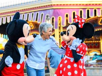 An older woman smiling with Mickey and Minnie