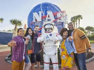 A group of 5 adults posing in front of the NASA logo with an astronaut