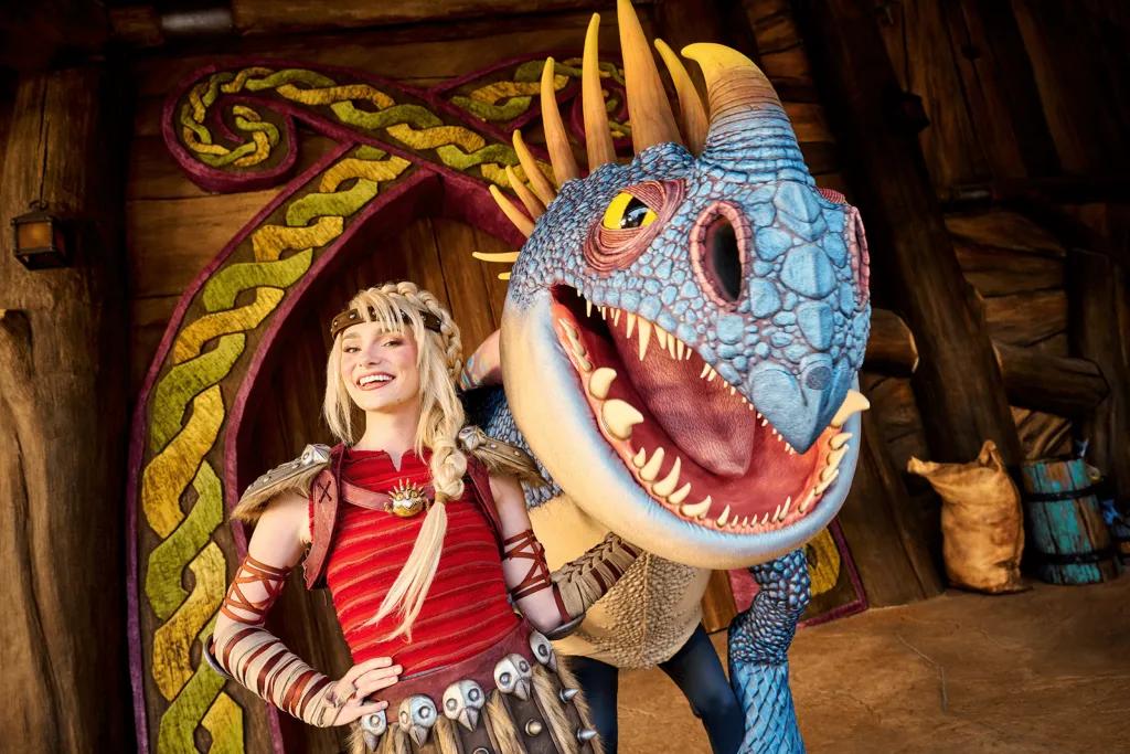 How to Train Your Dragon - Isle of Berk Astrid, a blonde Viking girl wearing skirt with skulls on it stood next to a blue and yellow dragon.