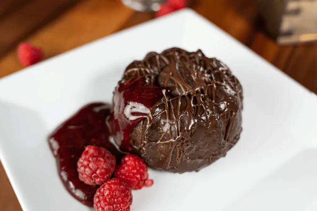 Chocolate Budnt Cake with Cranberry and Raspberry Sauce A small chocolate bundt cake on a plate with a raspberry and cranberry sauce