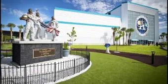 A statue of three astronauts holding an American flag in front of a building with a large sign reading Apollo NASA