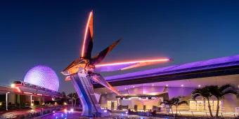 EPCOT, the guardians of a galaxy triangular space ship coloured yellow and grey. In the background there is a white golf ball shaped building and the monorail.