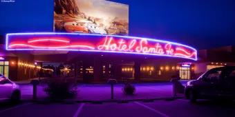 A neon sign reading Hotel Santa Fe underneath a large picture of Lightning McQueen and Sally from Cars