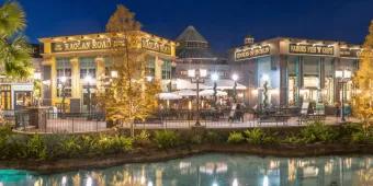 An Irish pub in Disney Springs coloured green and yellow labelled Raglan Road. Next door there is a fish and chips store. In front of these buildings there is a lake with crystal clear water.