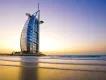Burj Al Arab Sail shaped building coloured white with many windows and a helicopter pad on top. It is in the middle of the ocean on a man made island, with one road connecting it with mainland.