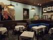 The Chef’s Table at The Edgewater Large blue room with dark decor, paintings and tables with white tablecloths inside.