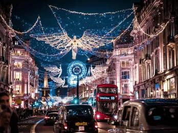 Black taxis and a red London bus driving down Oxford Street underneath the Christmas lights