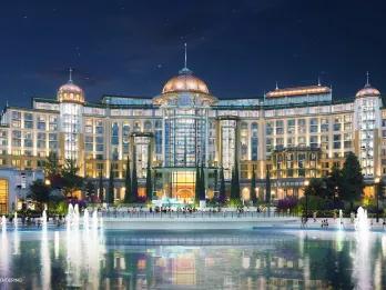 Large white building with rounded shape around large fountains. On top there are circular details on the roof that are golden with turquoise spikes on top. Looks very modern.