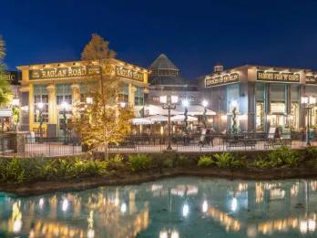 An Irish pub in Disney Springs coloured green and yellow labelled Raglan Road. Next door there is a fish and chips store. In front of these buildings there is a lake with crystal clear water.