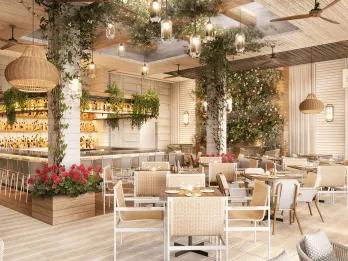 A pristine white restaurant with white and beige chairs and small square tables. Around there are purple flowers in wooden boxes and leaves hanging from the ceiling and decorated around the white beams. It looks very modern with low hanging circular lights.