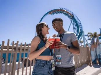 A couple posing with drinks in front of the Pipeline rollercoaster at SeaWorld