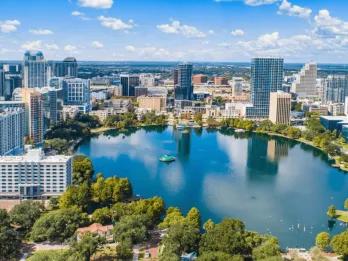 Modern buildings surrounding a large lake. Including a mix of smaller buildings and tall towers.