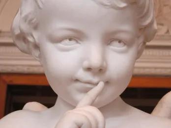 Statue of cupid (young boy) holding finger to lips as if to say shhhh with a mischevious expression