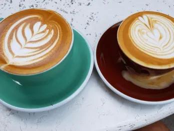 Two coffee cups with designs on top in mugs, one mint and the other dark red.